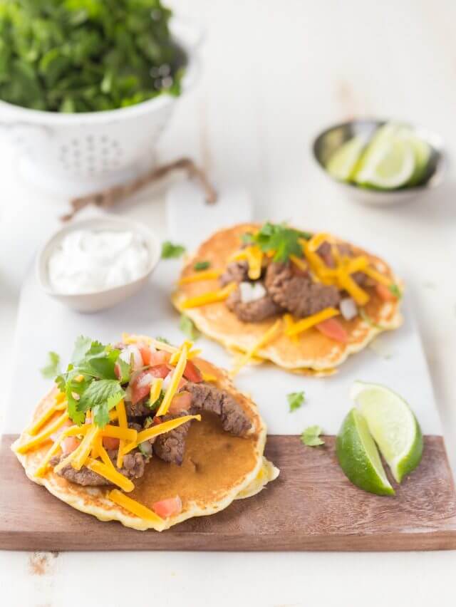 steak, parsley and cheese on top of a corn filled pancake on top of a white cutting board for display