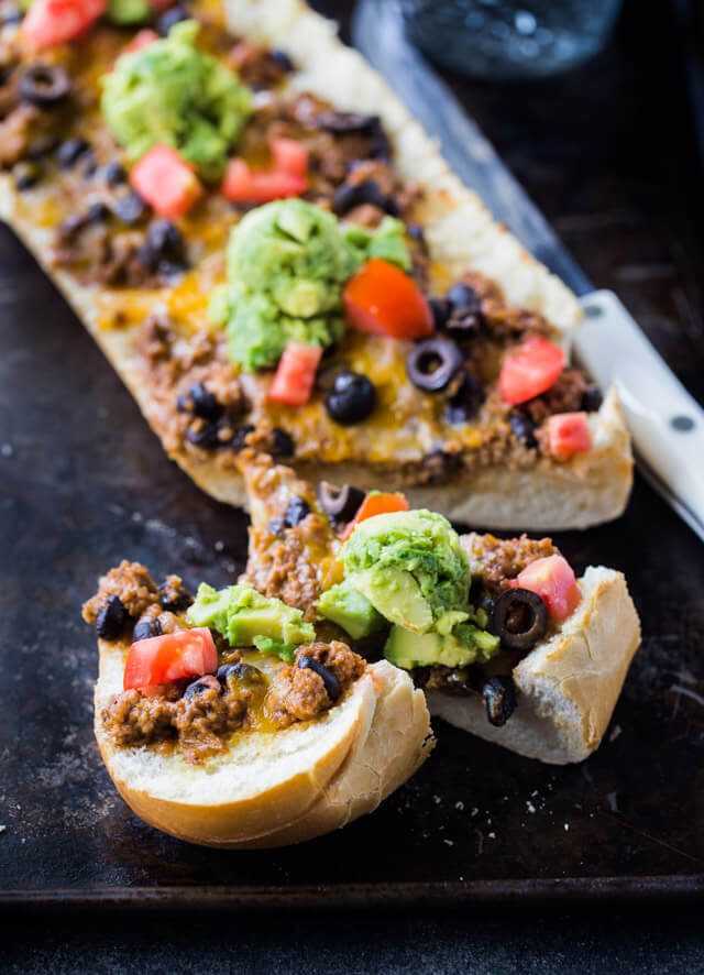 taco meat, avocado, tomatoes, olives and cheese on top of french bread