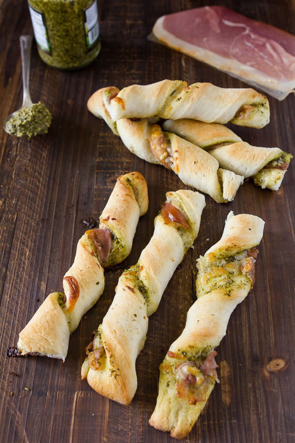 prosciutto pesto pizza twists with them lined on a board with a spoonful of pesto 
