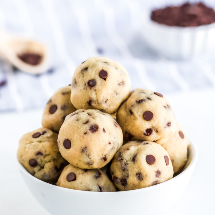 cookie dough balls in a white bowl with chocolate chips in the background