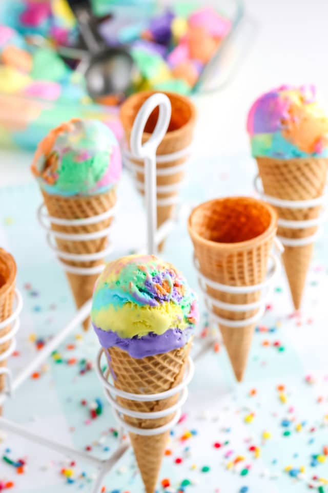 Rainbow ice cream in cones with a white stand with confetti